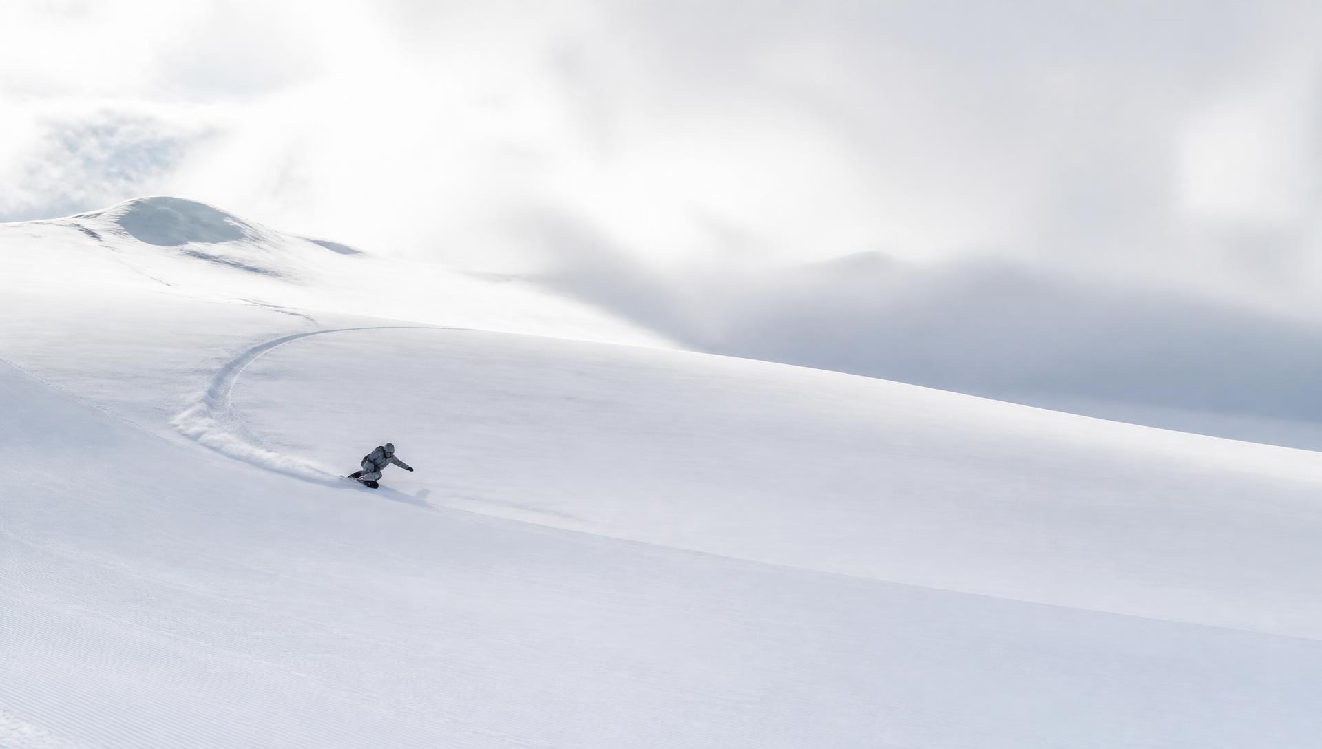 Snowboarder carving a clean arc across an empty alpine slope